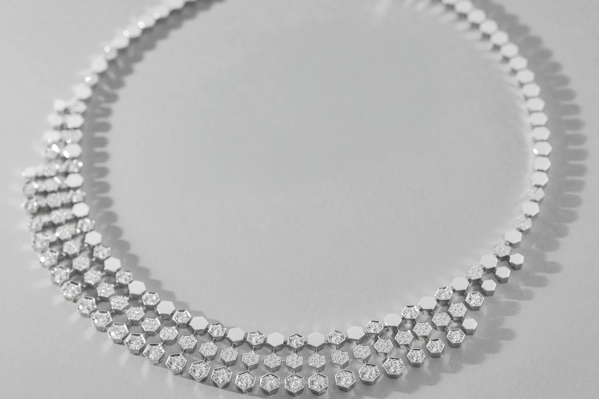 Collier plastron Bee de Chaumet aux maillons alvéolés sertis de diamants, posé à plat sur un fond gris
