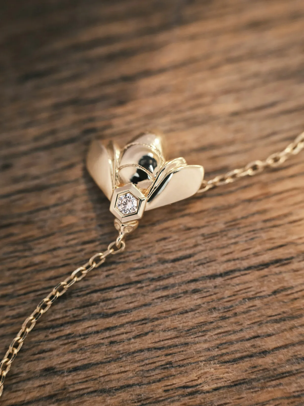 Pendentif Bee de Chaumet en or sur sa chaîne fine, posé sur un plateau de bois
