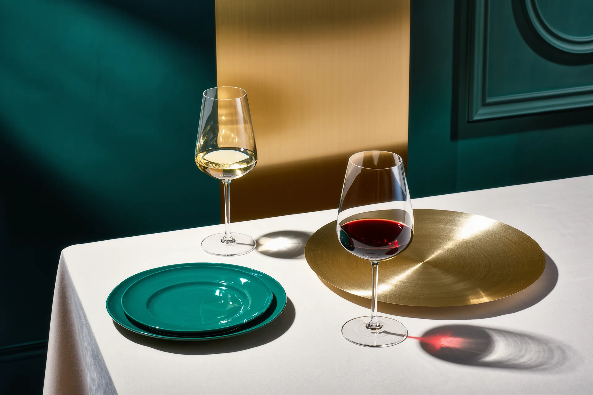 Un verre de vin blanc et un verre de vin rouge posés près de deux assiettes contrastées sur une nappe claire