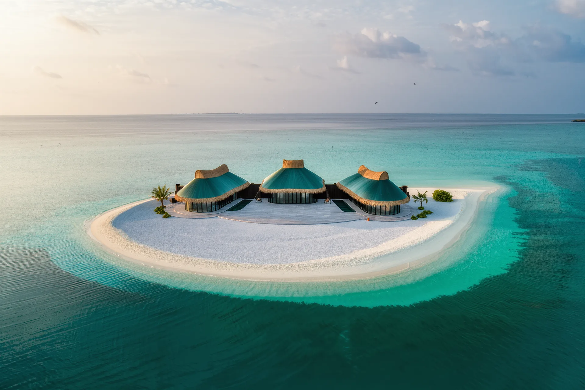 Une petite île tropicale vue du ciel, ceinte d'un lagon turquoise et coiffée de quelques toits de chaume.