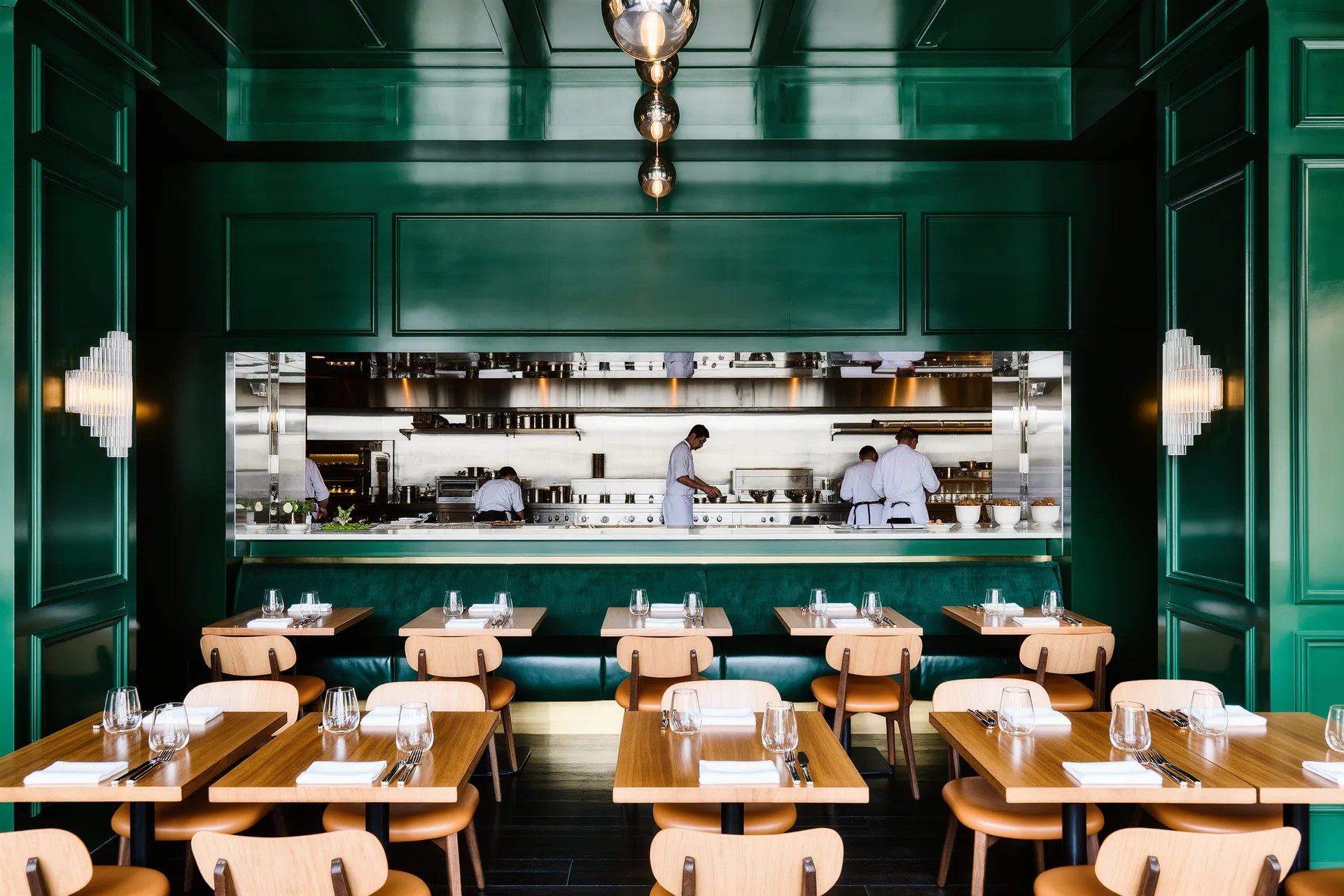 Petite salle de bistrot animée, tables nues en bois et cuisine ouverte au fond